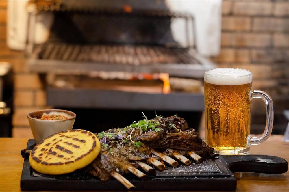 Grilled arepa served with grilled lamb ribs and a cold beer by the parrilla
