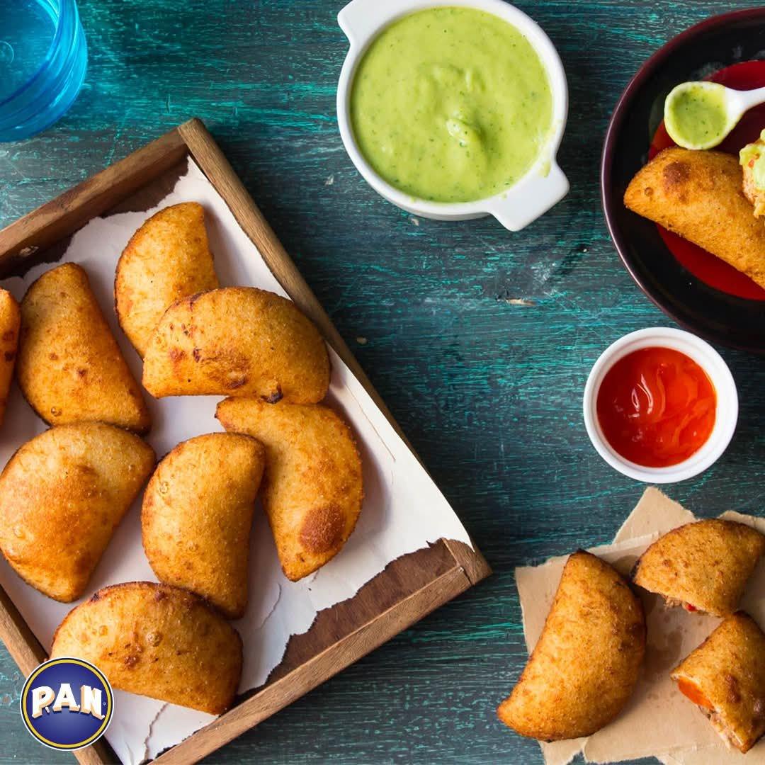 Tray of golden corn empanadas with green and red dipping sauces