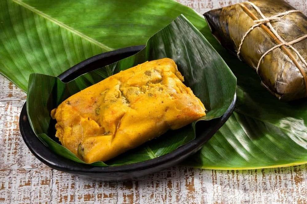 Cooked Colombian tamal unwrapped in dish on banana leaf